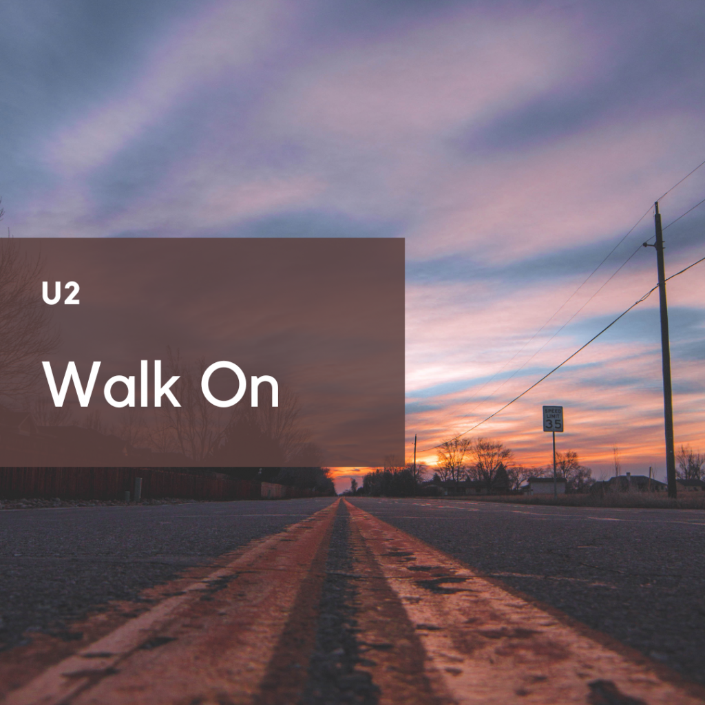 A stretch of roadway at sunrise with an offset brown square on the left. Words in white read "U2" and "Walk On"