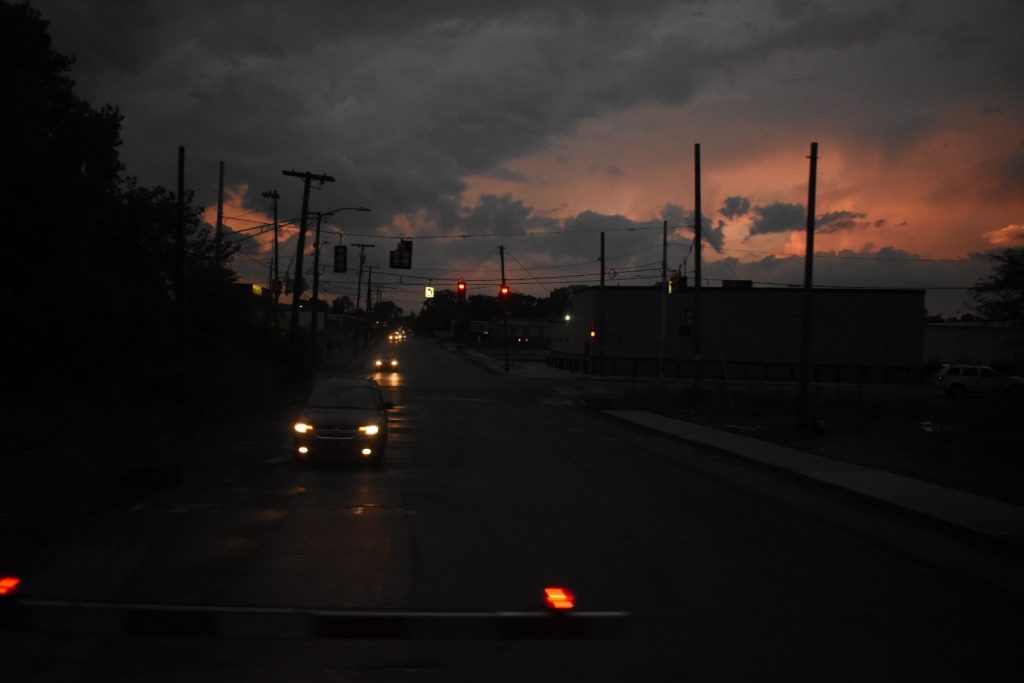 Moody sunset over a darkened street where cars wait at a railroad crossing 