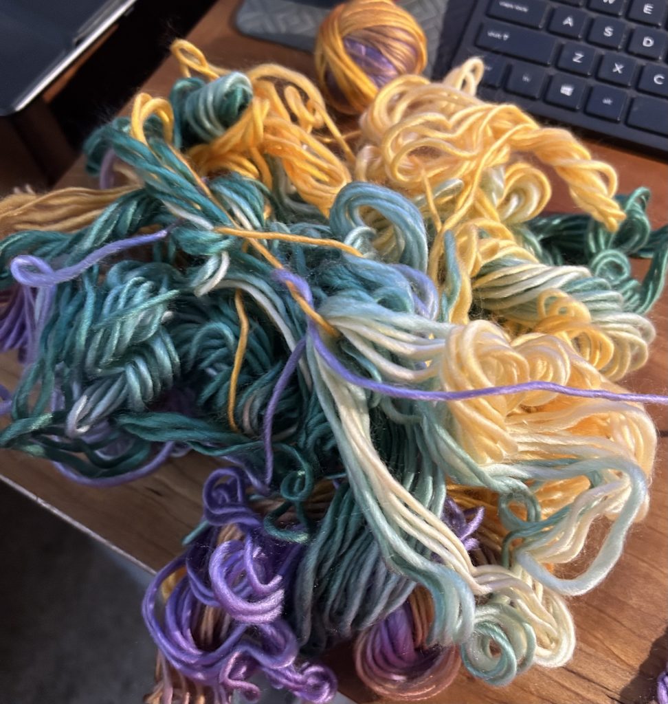 A tangle of yellow, goldenrod, lavender, green, aqua, and purple yarn.