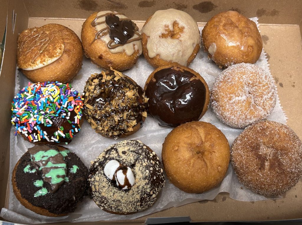 A box of a dozen doughnuts with various toppings, no two the same.