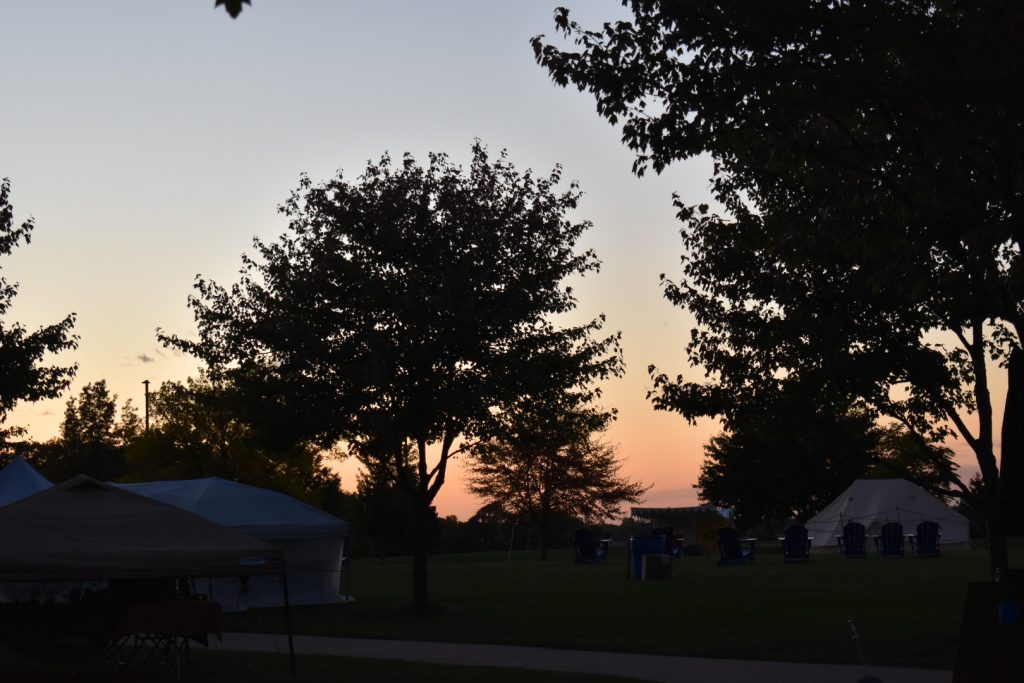 A sunset with trees and festival tents in the foreground.