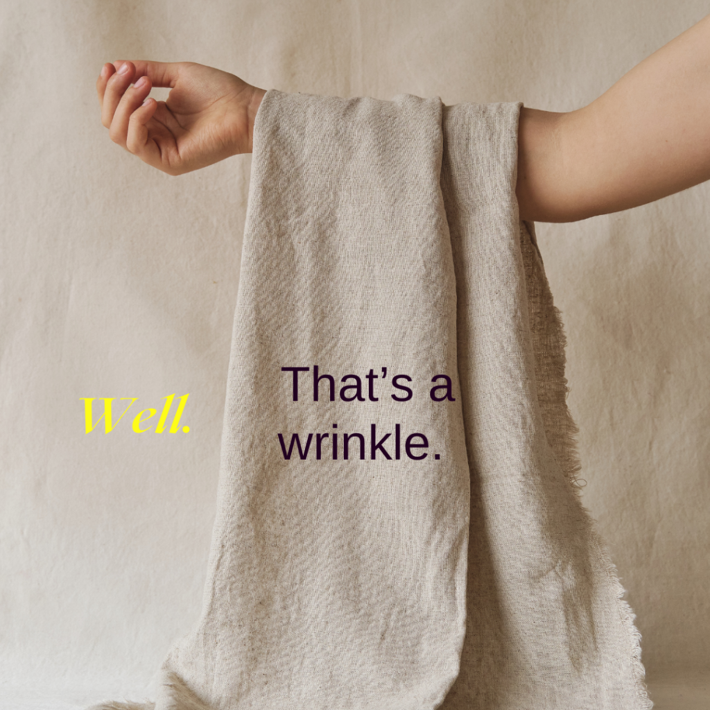 An arm holding a beige piece of woven fabric. Words over the image read “Well.  That’s a wrinkle.”