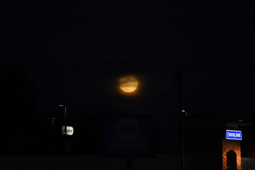 Orange-yellow full moon obscured by clouds in a a suburban landscape