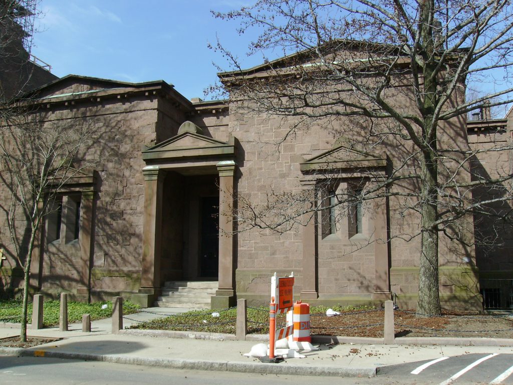 An old brown brick building with a doorway sunken in shadows on a modern city street.