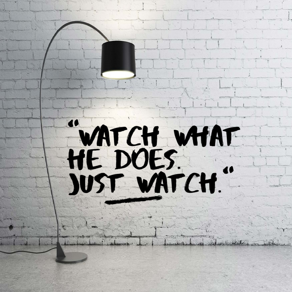 White washed brick wall background and a white floor with a black floor lamp in front.  Words in black: "Watch what he does. Just watch."