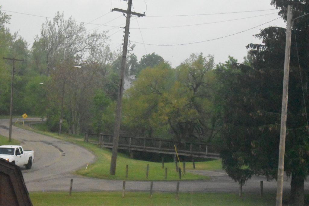 Rural road and power lines with a wooden bridge and trees.
