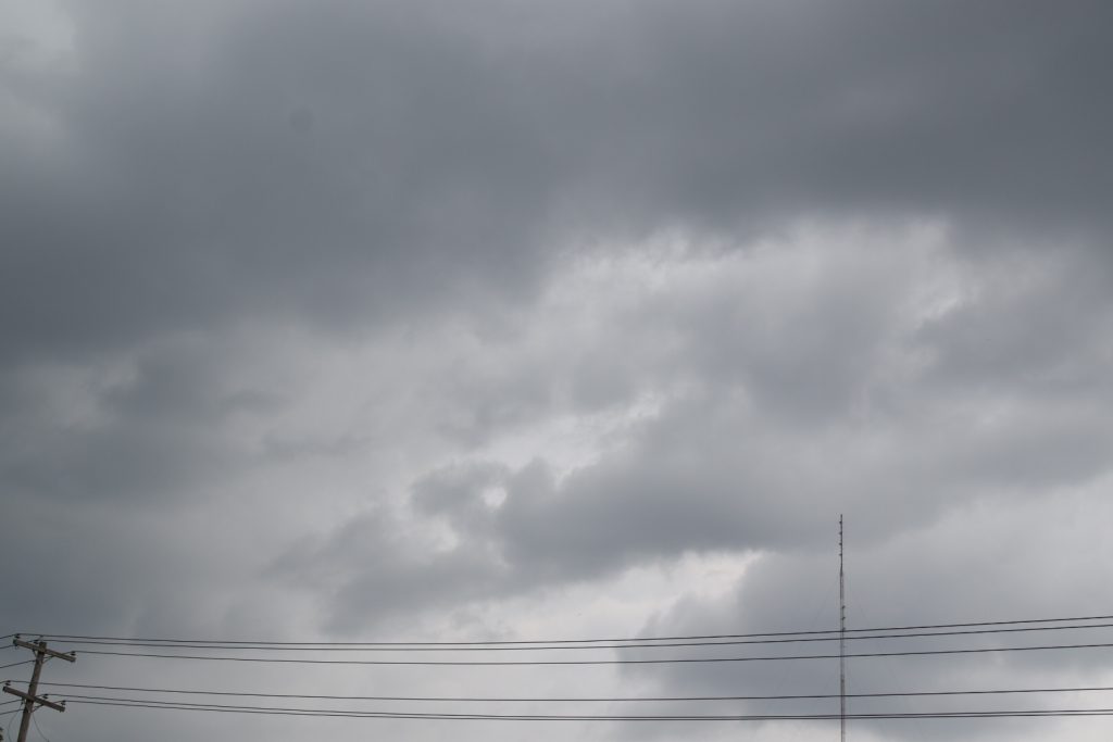 Storm clouds in the sky with a radio tower and power lines in the bottom foreground.